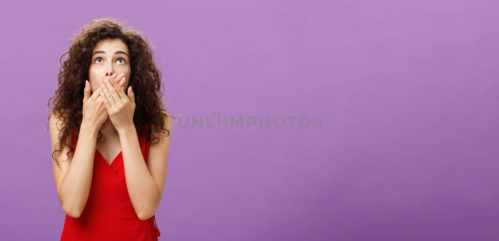 Woman being shocked and stunned seing guy about fall down. from tree gasping feeling nervous covering opened from amazement mouth looking up standing intense over purple background in evening red dress.