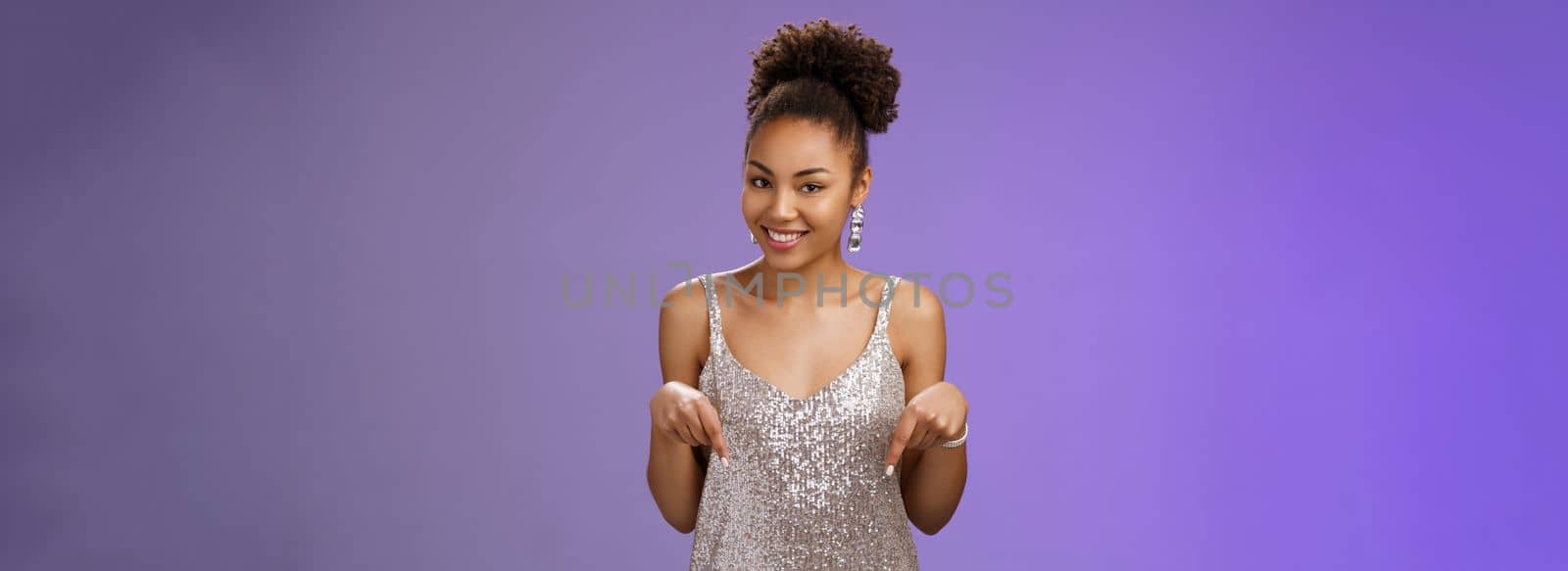 Stylish confident flirty elegant african-american young woman glamour shiny silver dress pointing up index fingers smiling camera assertive suggesting perfect accessorise for your outfit by Benzoix