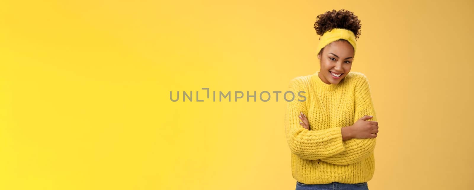 Tender delicate young african-american cheerful girlfriend curly hairstyle headband sweater hugging herself embracing gladly smiling camera feel soft comfortable, standing yellow background warm.