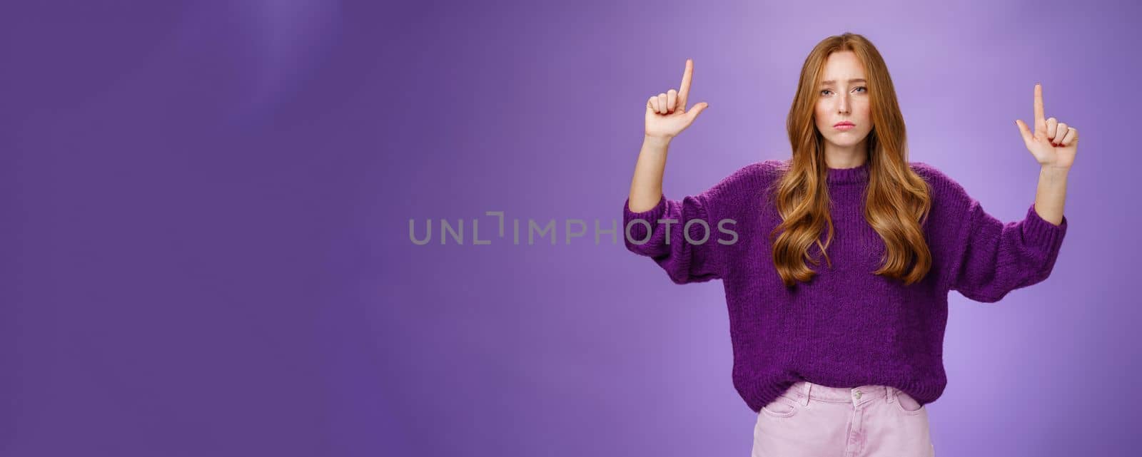 Disappointed gloomy and moody attractive redhead woman with freckles in warm sweater raising hands pointing up and reacting with sadness and regret on product or copy space, being unsatisfied, unhappy.