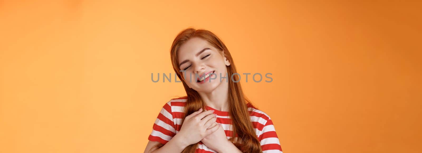 Close-up lovely caring tender redhead girlfriend feel love, close eyes smiling toothy silly grin, press palms heart, feel touched, daydreaming, have feelings, confess sympathy tasty food.