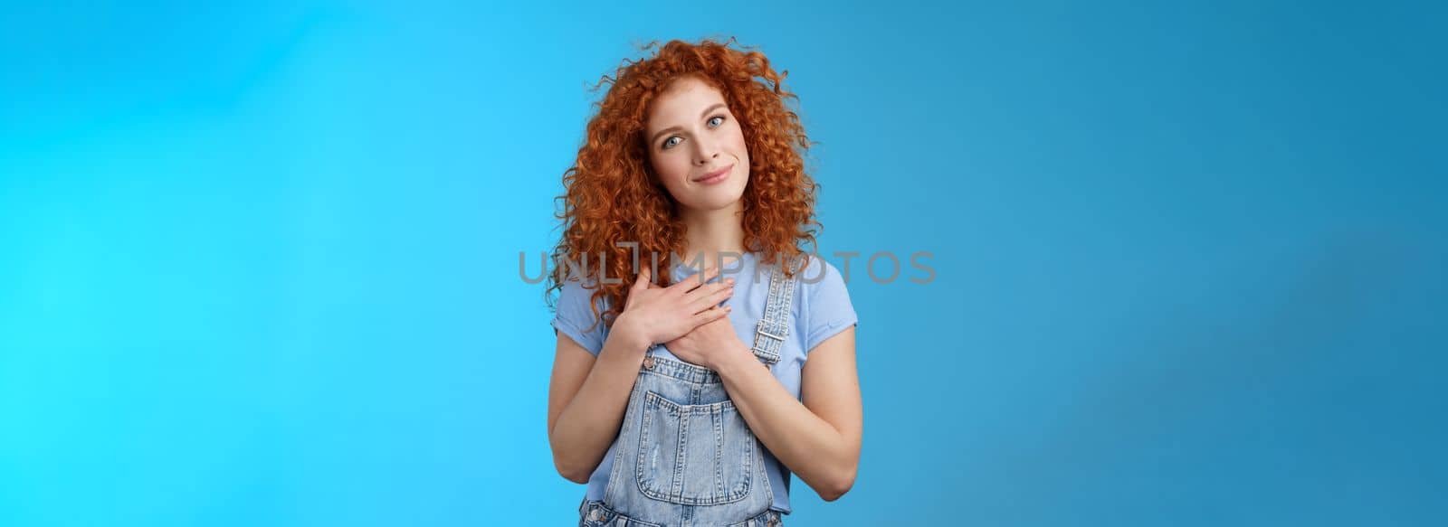 Lifestyle. Cute tender attractive redhead curly girl cherish romantic feelings thankful pleasant gift touch heart press palms chest grateful smiling broadly tilt head pleased feel loving caring emotions.