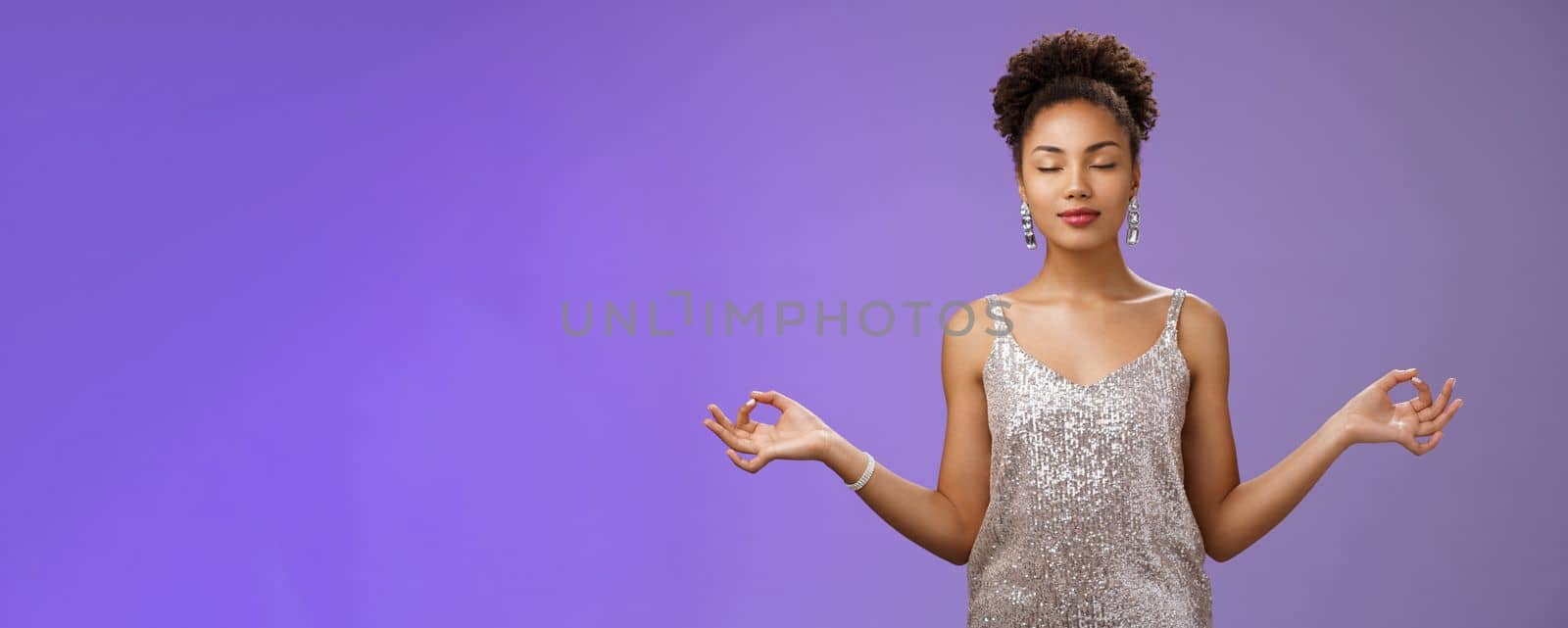 Peaceful confident relieved african-american young woman elegant silver dress calm down meditating close eyes breathing practice standing nirvana lotus yoga pose find zen, blue background by Benzoix