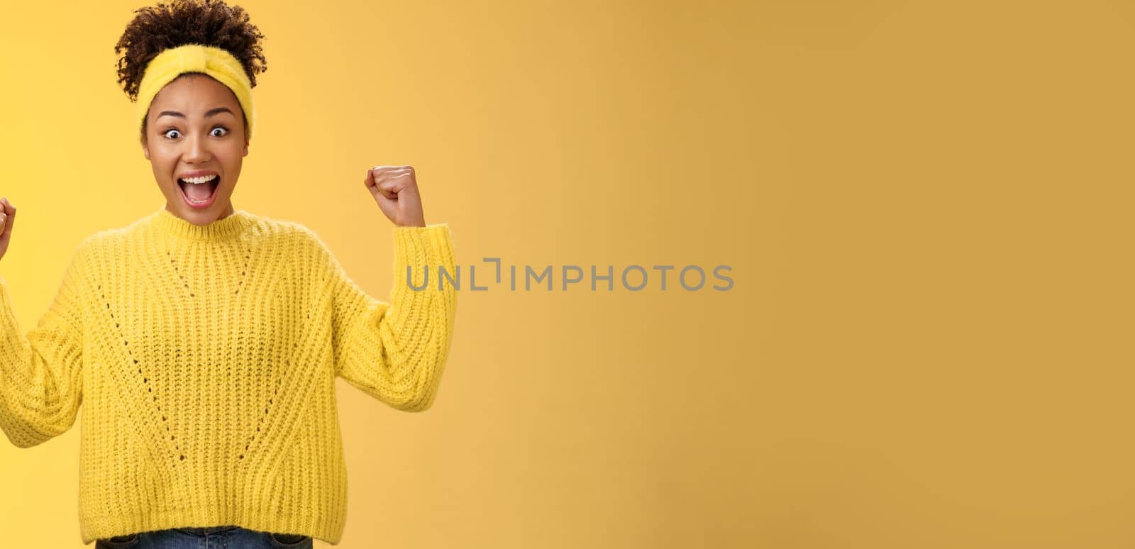 Yes finally prize mine. Excited surprised amused african-american girl celebrating victory achivement cheering smiling broadly yelling rest fists triumphing success, standing yellow background by Benzoix