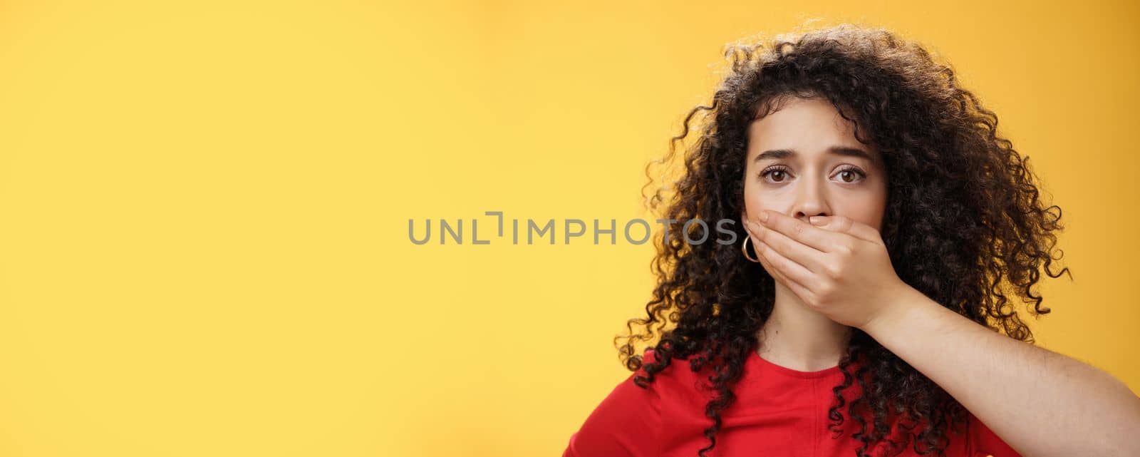 Lifestyle. Close-up shot of concerned and insecure troubled woman keep silent scare of telling anyone her problem covering mouth with palm not to scream or slip word looking sad and sorrow over yellow background.