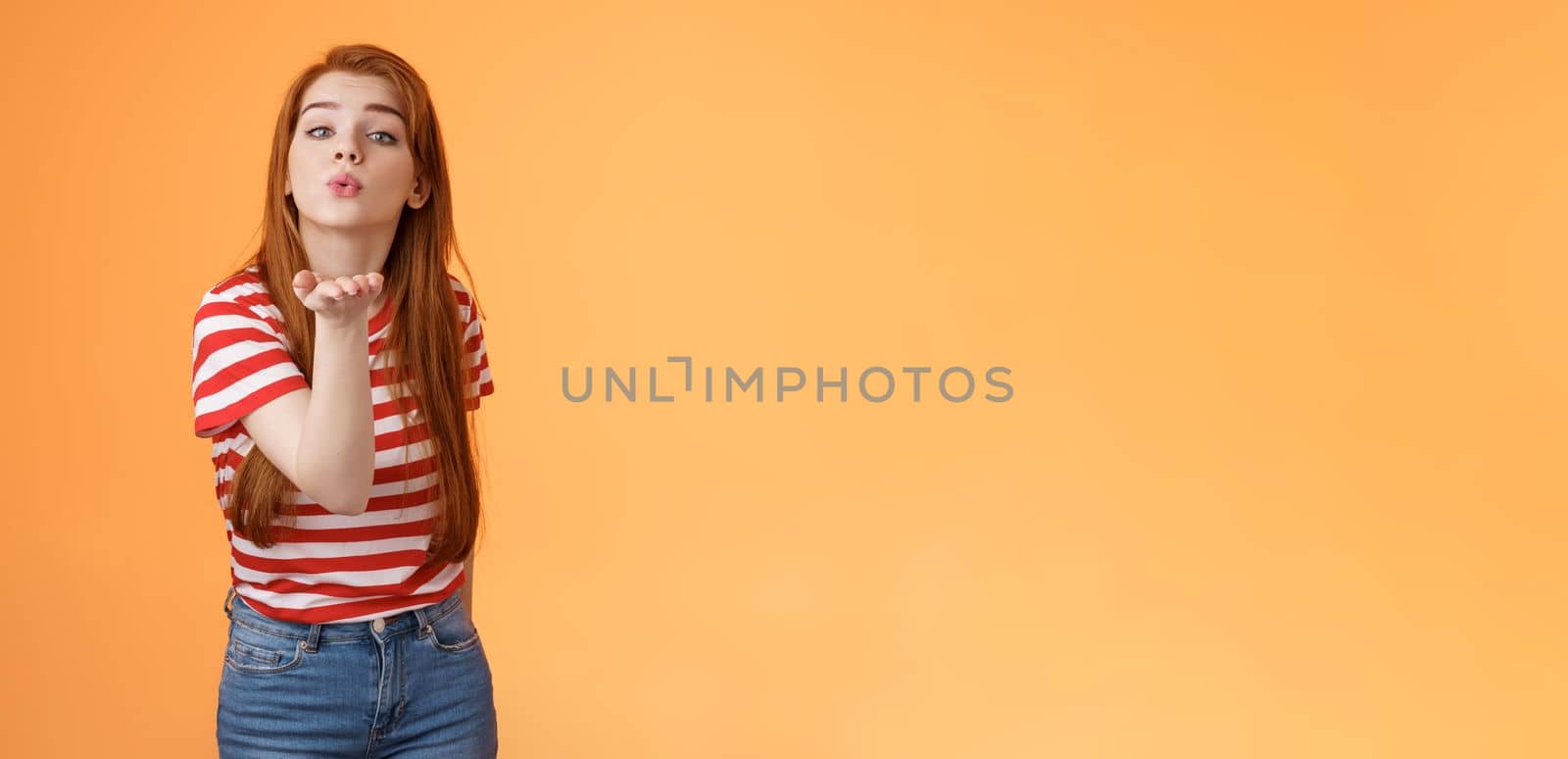 Silly cute and flirty redhead passionate girl, send air kiss camera, fold lips hold arm near mouth to blow mwah, romantic tender attitude, confess love like guy, stand orange background by Benzoix