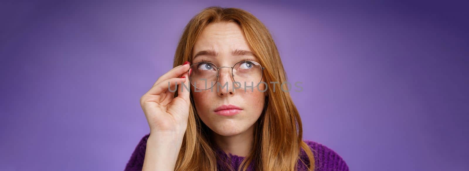 Clumsy and cute young female teacher in glasses with red hair looking unsure and confused looking interested at upper left corner touching rim of glasses thinking or picturing in imagination by Benzoix