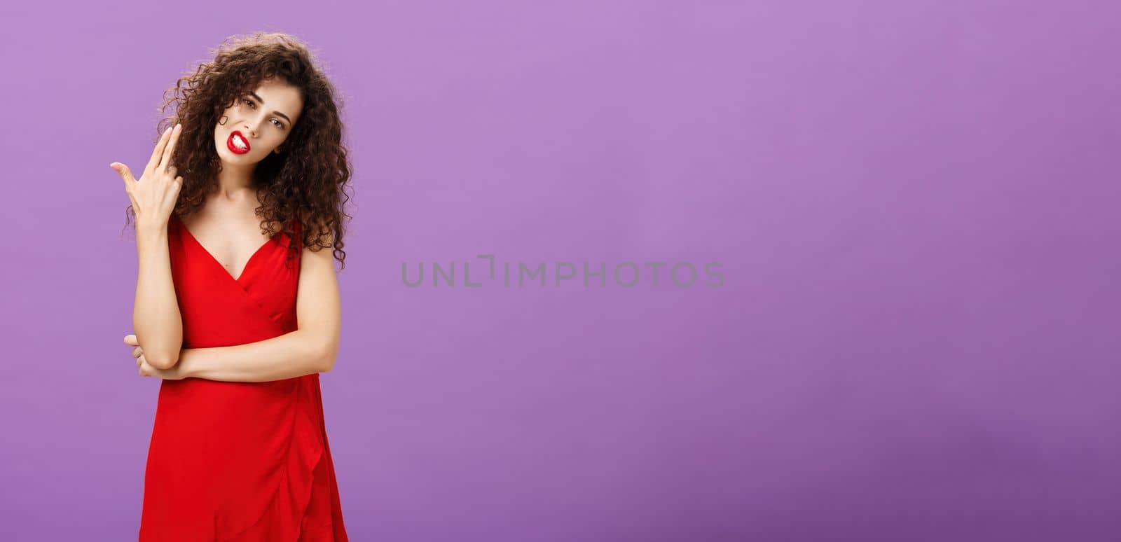 Rules killing me. Rebellious hot and stylish european woman in elegant red dress with curly hairstyle tilting head showing finger gun gesture as if blowing brains from boredom over purple background. Emotions concept