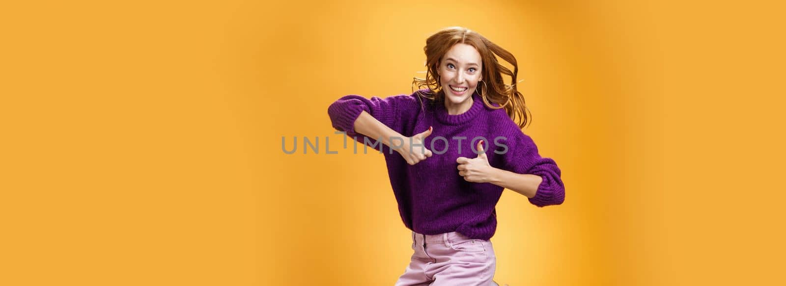 Optimistic and cheerful woman liking promotion lifting thumbs up and jumping from excitement and delighted, having fun recommending good idea smiling thrilled and enthusiastic over orange background by Benzoix