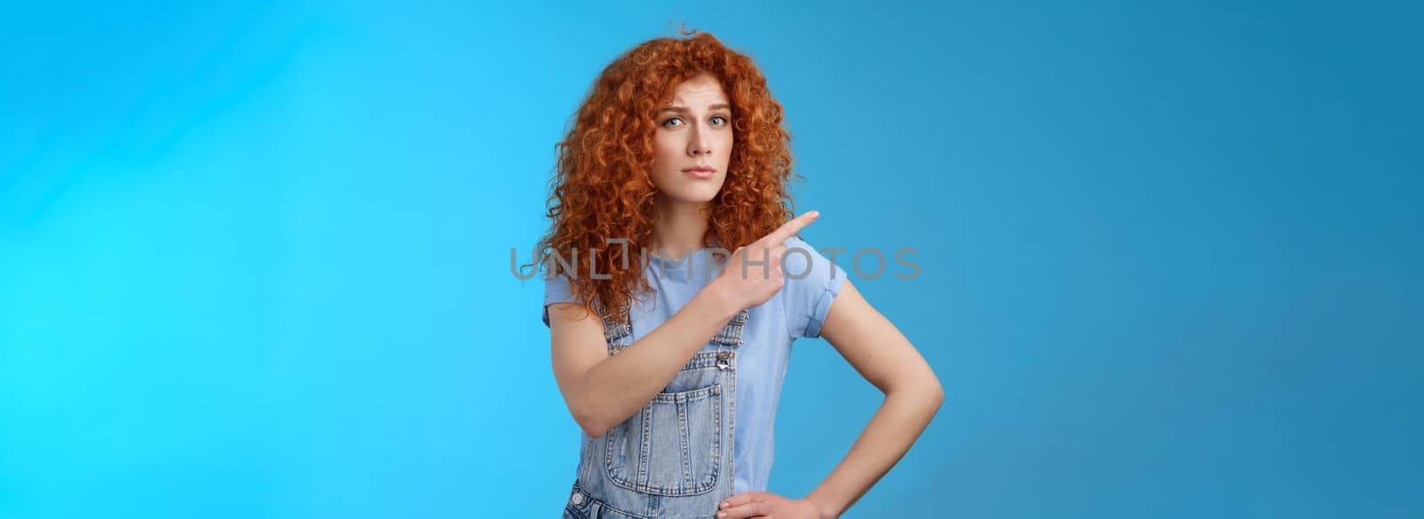 Lifestyle. Unsure silly timid hesitant cute redhead curly-haired ginger girl frowning uncertain asking your opinion questioned look camera pointing upper left corner confused worried blue background.