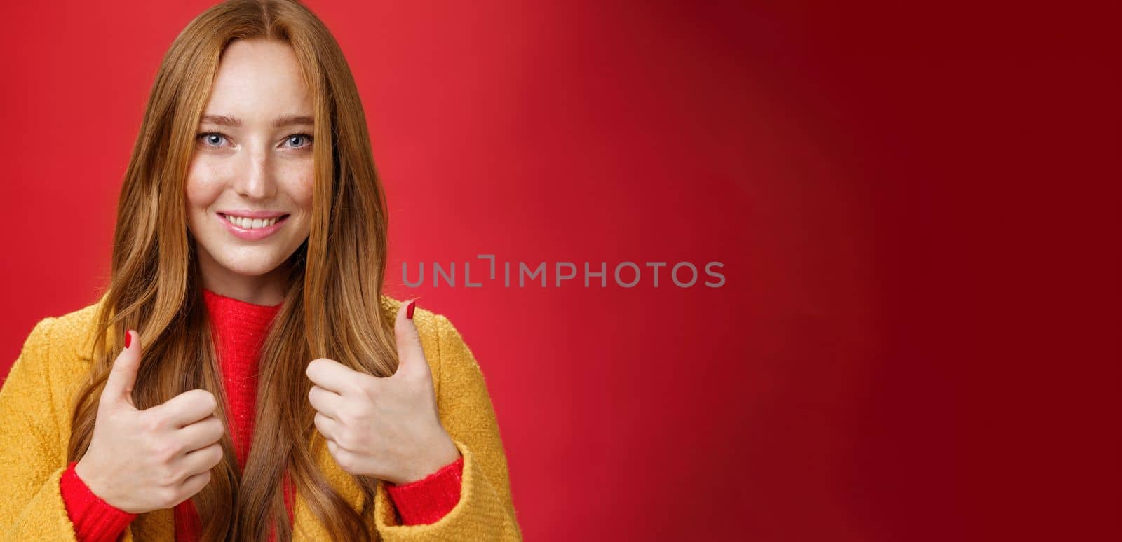 Close-up shot of satisfied happy young 20s woman in yellow coat showing thumbs up gesture in like and approval giving positive feedback enjoying nice event standing over red background, smiling cute by Benzoix