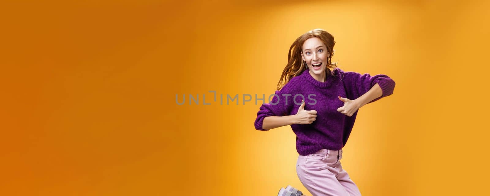 Excited and happy funny young redhead female in purple sweater jumping from happiness and satisfacion showing thumbs up gesture in approval giving positive reply and liking awesome clothes by Benzoix