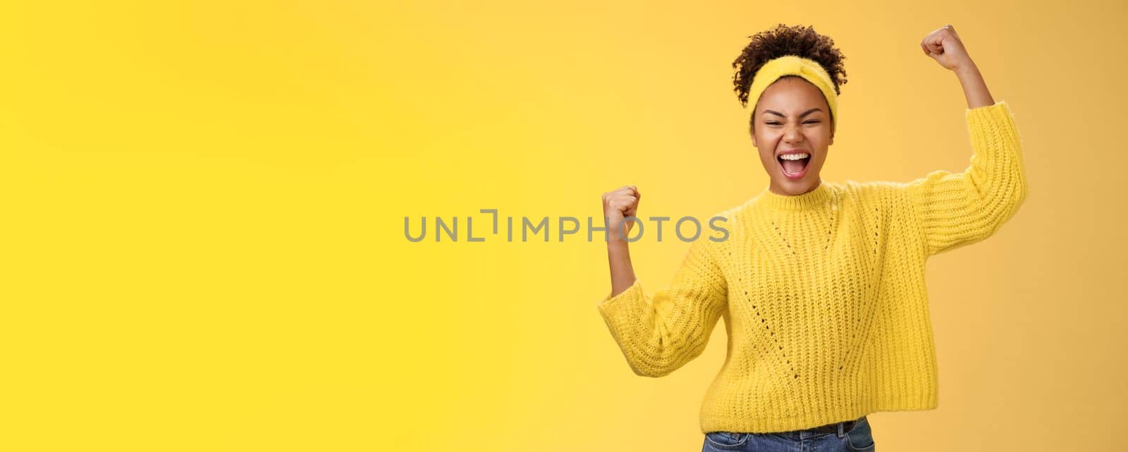 Active outgoing confident cheerful african-american female fan place bet hopefully yelling encourage team win standing raised fists victory celebrating gesture shouting proudly, yellow background.