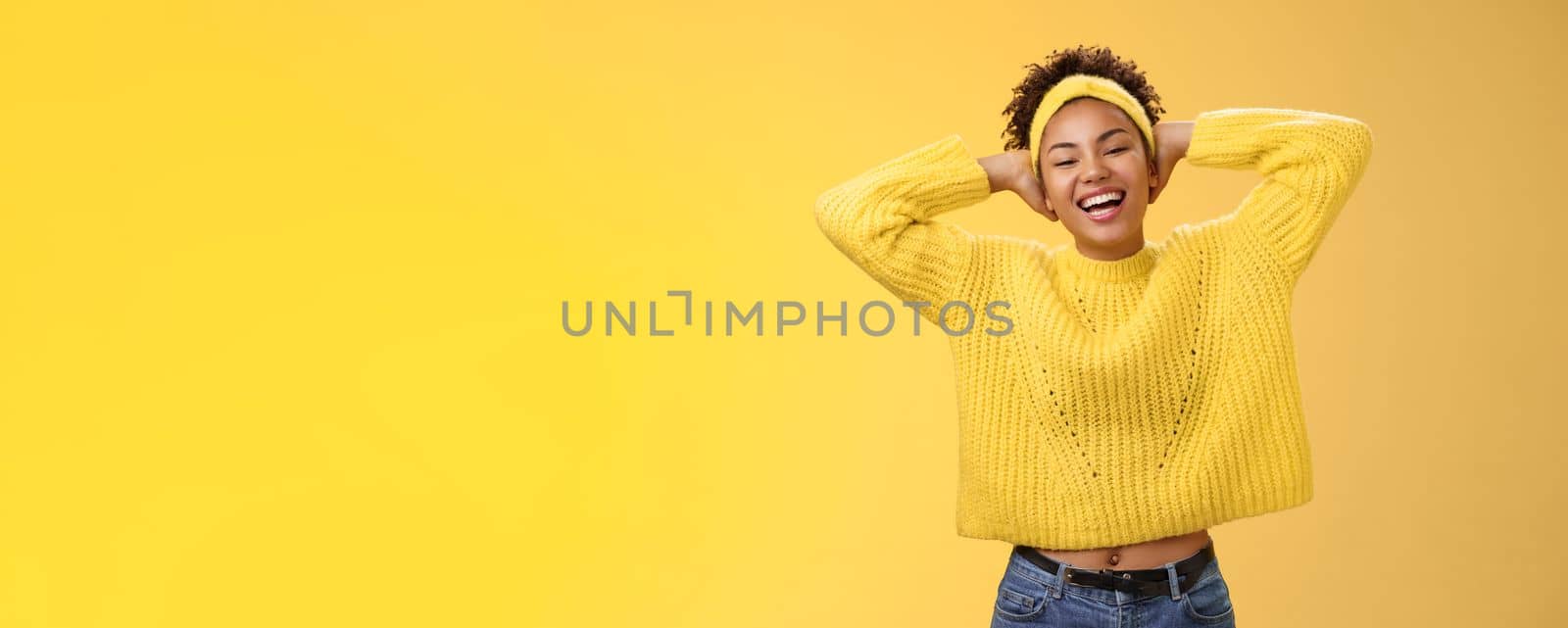 Carefree joyful lucky african-american female student in sweater headband lay back hands behind head relaxed chilling pose having day-off weekend smiling broadly laughing, yellow background.