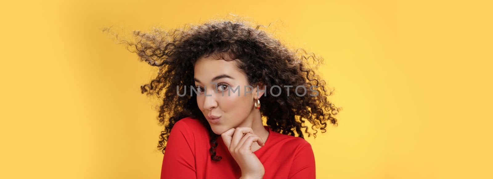 Cute flirty and silly female making coquettish gazed at camera folding lips feminine turning head and touching chin as seducing while hair curls waving in air expressing foreplay and romantic attitude by Benzoix