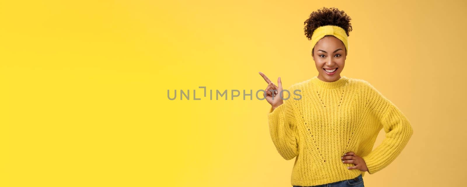 Charming sassy stylish african-american girl in sweater pointing upper left corner standing confident cheeky energized smile yellow background promoting merch showing best choice look camera amused by Benzoix