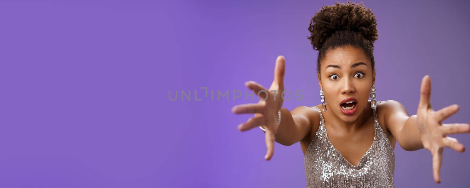 Stylish confused african woman in silver shiny dress cringing worried extend arms forward concerned standing perplexed panicking falling during night club, standing blue background. Copy space