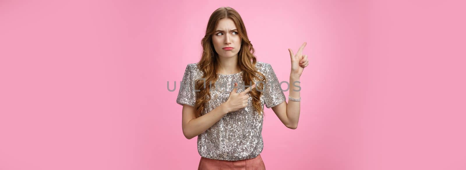 Displeased arrogant snobbish young rich glamour girl looking displeased cringe pointing left sideways, dislike place standing awkward insecure, expressing aversion reluctance, pink background.