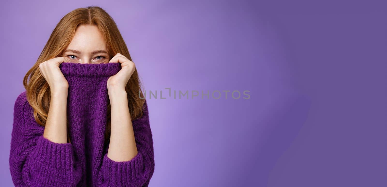 Lifestyle. Girl awaits winter with happy grin being ready warming up with cozy sweater pulling collar on face and smiling with eyes at camera standing positive and cute against purple background.