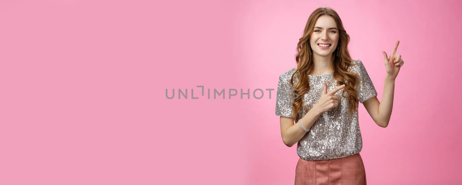 Lifestyle. Studio shot friendly-looking joyful smiling pretty european woman curly hairstyle party clothes inviting friends come in pointing upper right corner grinning happily having fun show advertisement.