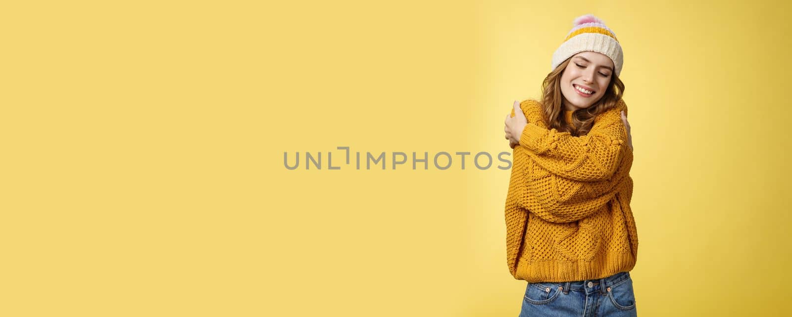 Tenderness, happiness wellbeing concept. Charming feminine cute stylish girl liking new warm sweater hugging embracing herself close eyes dreamy smiling feeling romantic coziness yellow background by Benzoix