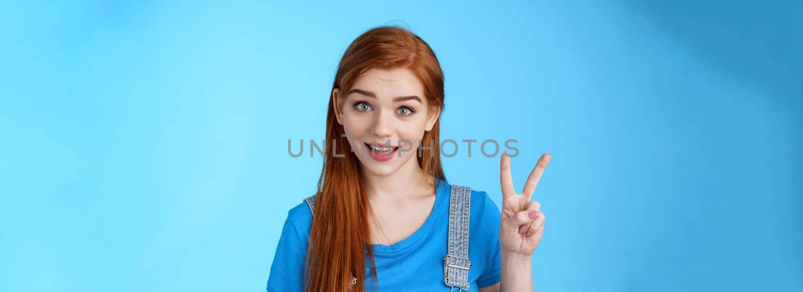 Cheerful attractive redhead caucasian girl smiling joyfully talking, order two peaces, show second number, peace victory sign, stand carefree, upbeat emotions, stand blue background by Benzoix