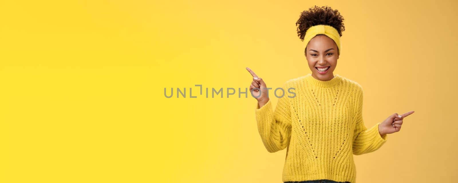 Charming tender romantic young african-american 20s woman smiling friendly satisfied laughing lovely look camera pointing up right sideways show products choices two ways, standing yellow background.