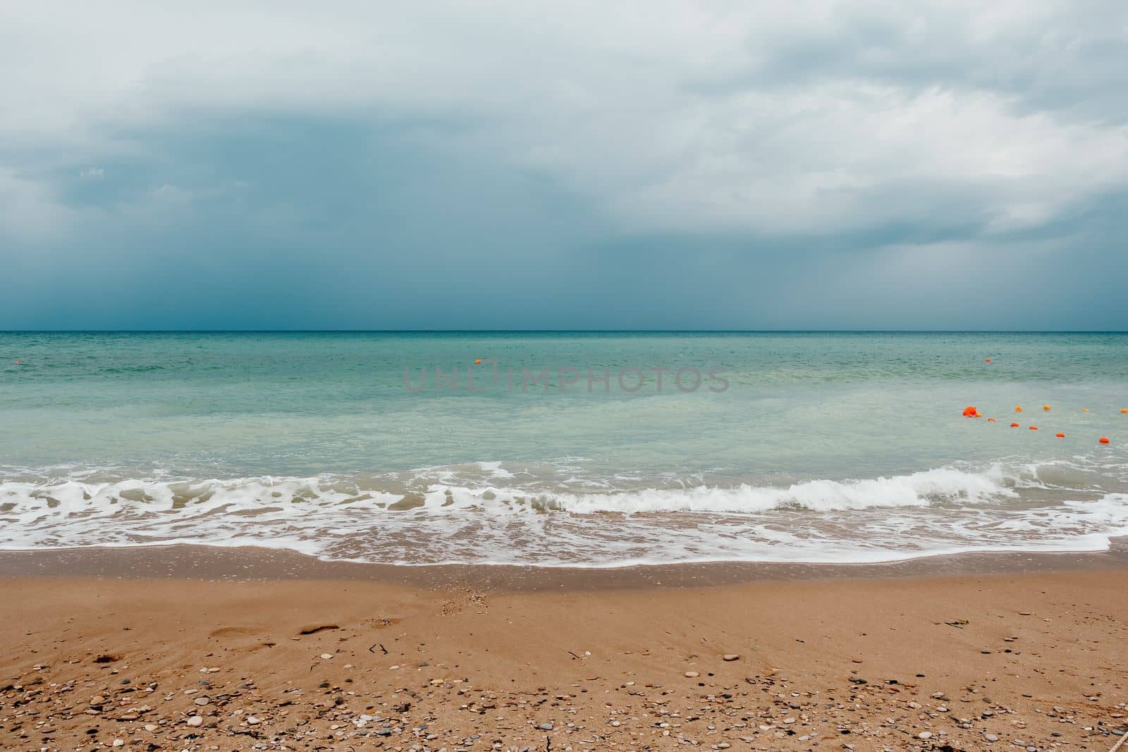 Overcast sky on rainy day with foamy waves rolling towards golden sand beach under low warm sun light. Nobody. Holiday recreation concept. Abstract nautical summer ocean sunset nature. by panophotograph