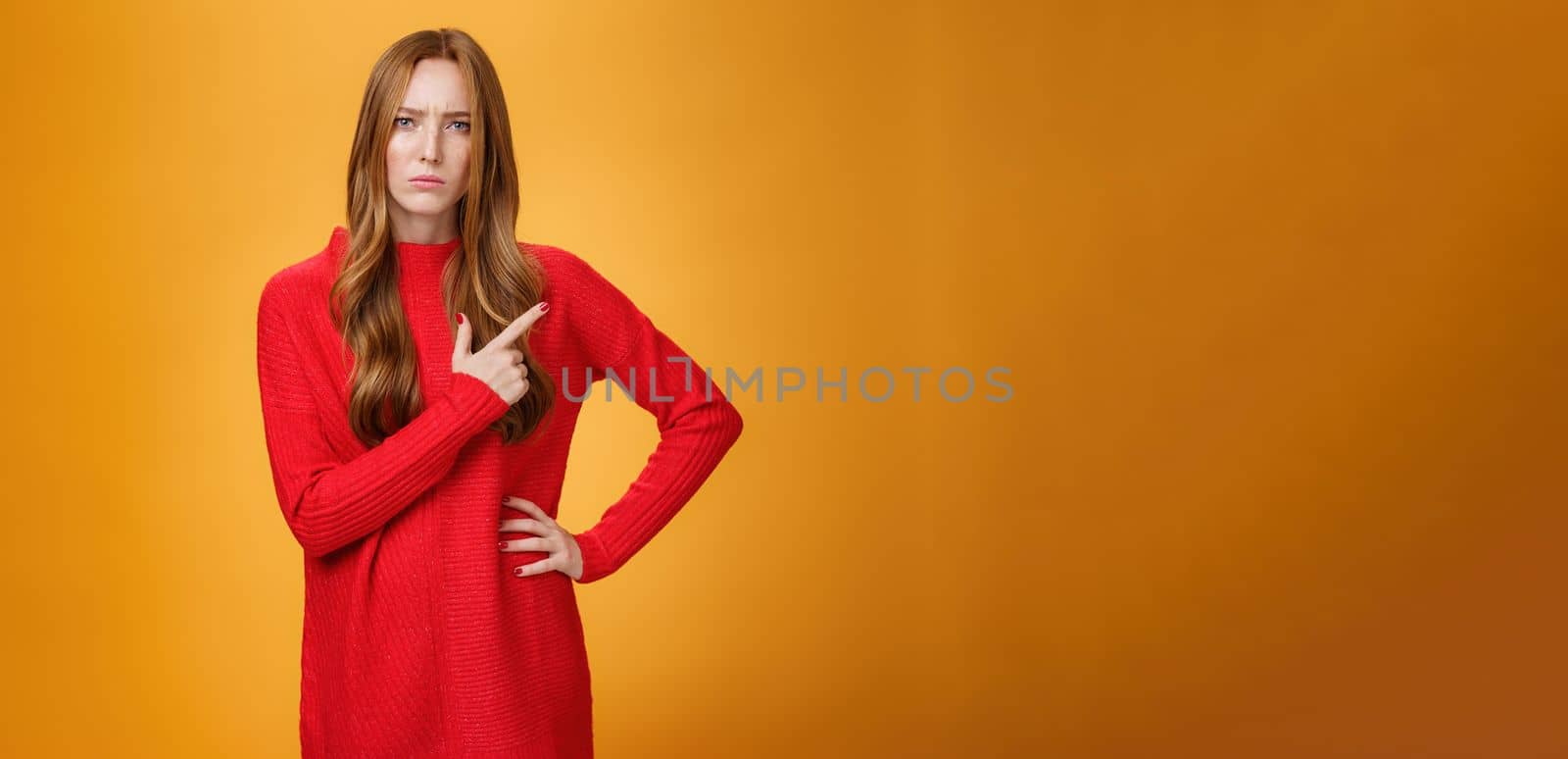 Girlfriend asking serious question being bothered by unfamiliar woman on family dinner pointing behind frowning and squinting suspicious expressing disbelief, doubt and vigilance over orange wall by Benzoix