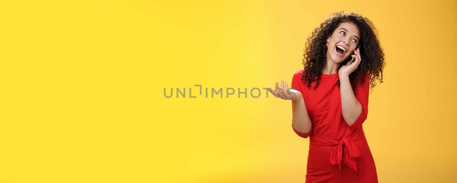 Lifestyle. Talkative glamour silly girl with curly hair having fun feeling carefree and happy taling on mobile phone turning away as laughing joyfully gesturing with hand holding smartphone pressed to ear.