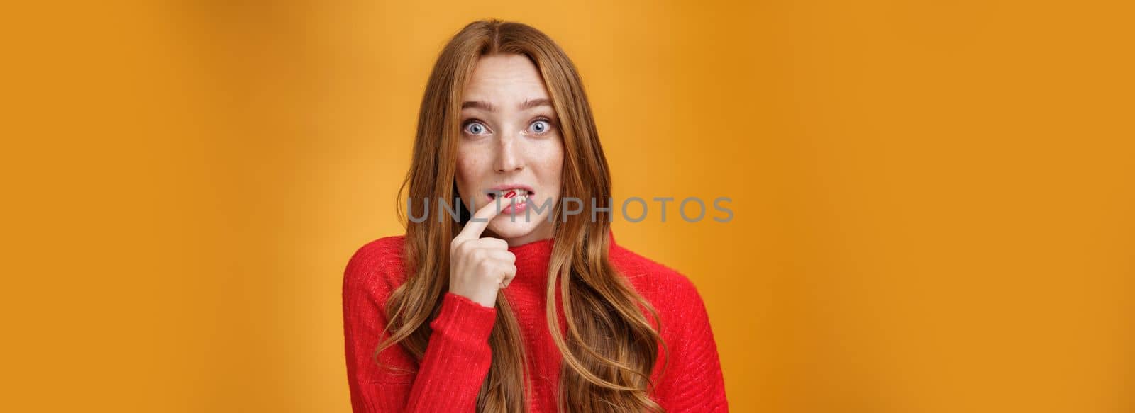 Silly, cute redhead woman making innocent oops expression holding finger on lip and looking scared with questioned expression at camera making mistake and trying get away of troubles with flirty gaze.