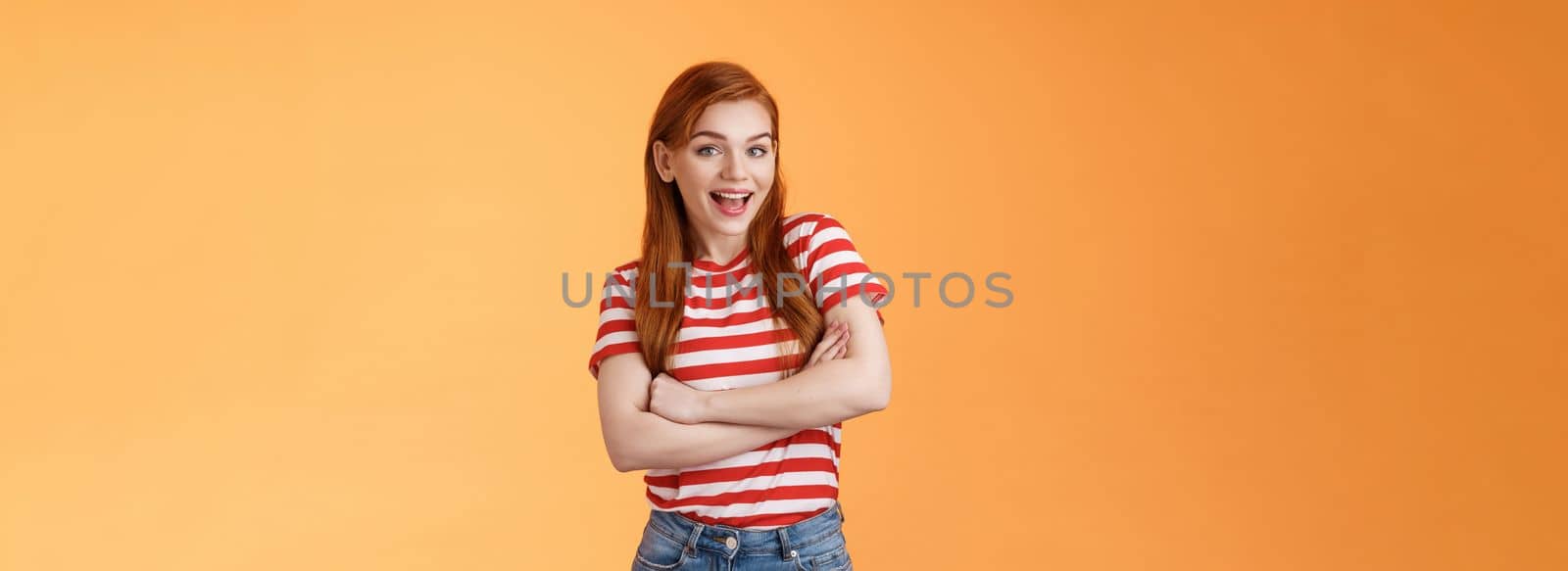 Excited cheerful ginger girl long natural red hair open mouth enthusiastic smile, cross arms chest, gladly react interesting awesome news, feel surprised pleased, stand orange background.