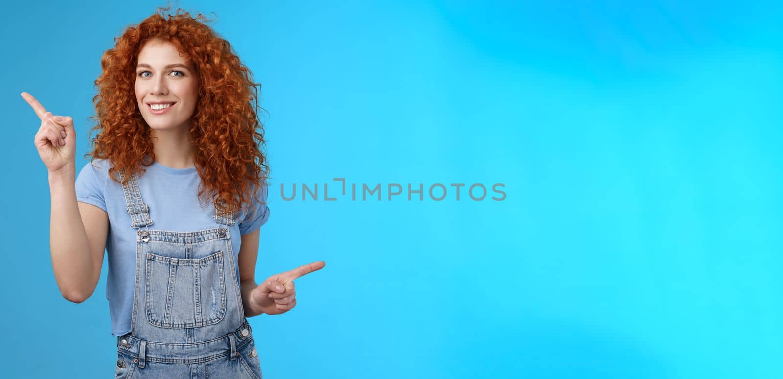 Lifestyle. Lively joyful good-looking 25s redhead curly-haired sassy girl summer positive mood dancing overalls pointing sideways up right index fingers directing promos store links smiling delighted.