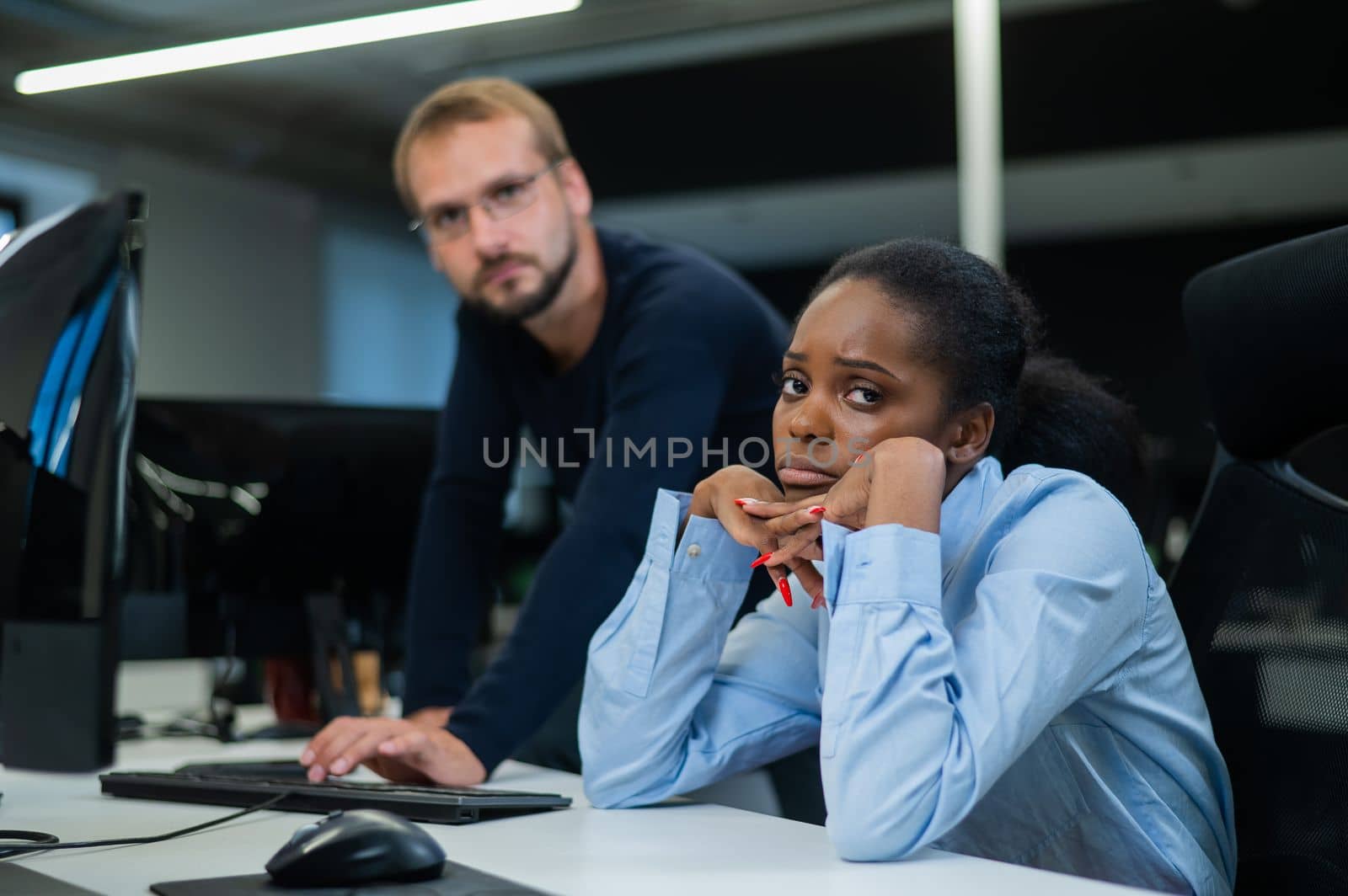 Colleagues look at the monitor and decide working moments. Caucasian man helps sad african woman solve computer problem