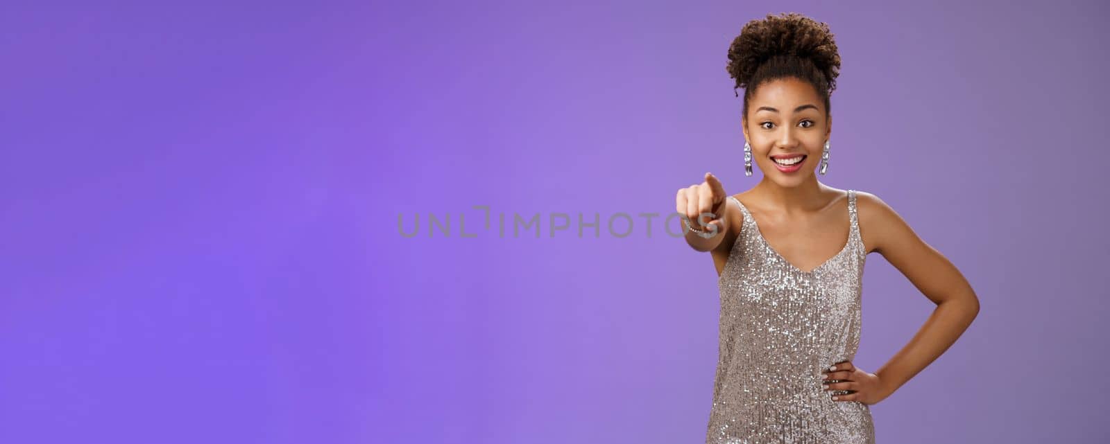 Joyful impressed african-american woman impolitely pointing camera indicating funny interesting person outfit smiling delighted staring thrilled joyful posing blue background. Copy space