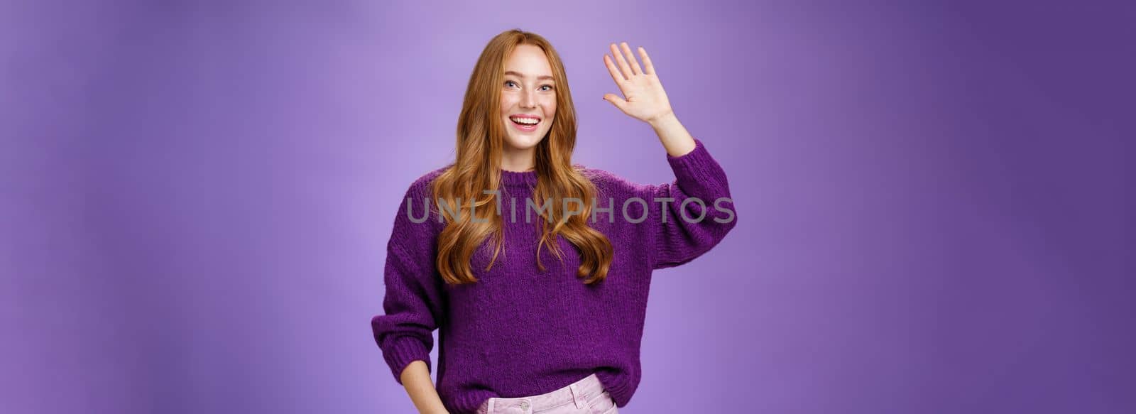 High five mate, hello. Portrait of friendly and excited charming kind redhead girl in sweater raising hand and waving in hi gesture, greeting best friend and smiling broadly as pleased meet by Benzoix