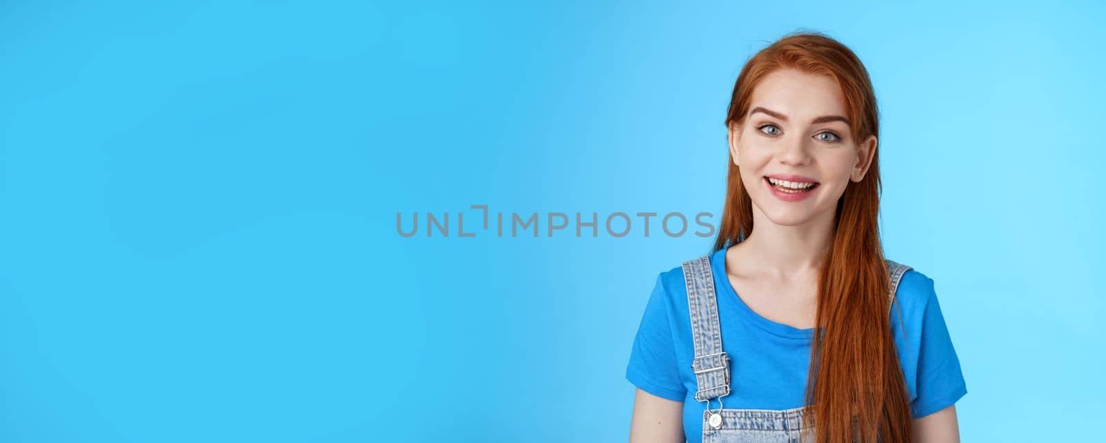 Friendly confident pleasant redhead woman helpfully look camera, smiling joyfully, have conversation customer, give advice, stand upbeat good positive mood blue background, grin amused by Benzoix