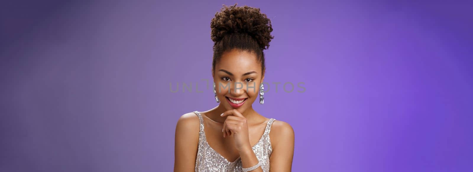 Intrigued creative young african-american devious 20s girl afro hairstyle in silver luxurious dress partying touching chin smirking mysterious have excellent idea inspired planning, blue background.