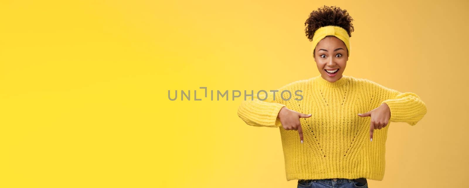 Enthusiastic impressed surprised beautiful african-american woman widen eyes drop jaw smiling gasping astonished pointing down amused standing yellow background showing amazing opportunity.
