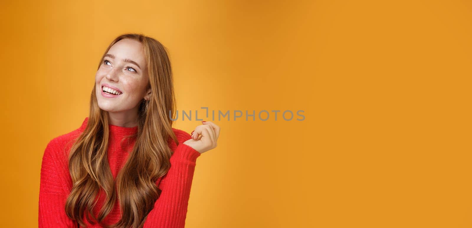 Close-up shot of nostalgic cute and sensual friendly-looking european female with nice cute memories looking at upper left corner dreamy and delighted, imaging and picturing desire over orange wall.