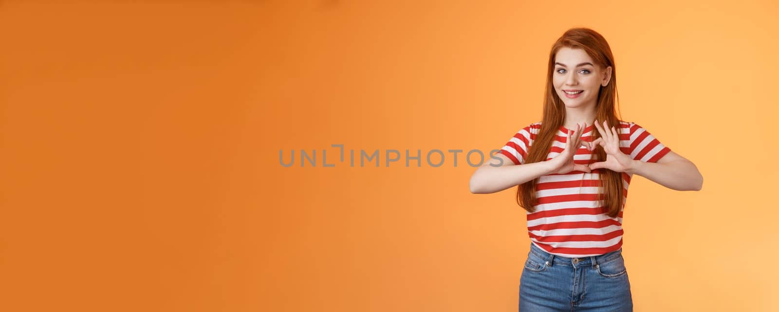 Cute lovely cheerful redhead girlfriend express love and cherish relationship, celebrating anniversary show heart sign, smiling tenderly, confess sympathy, stand orange background.