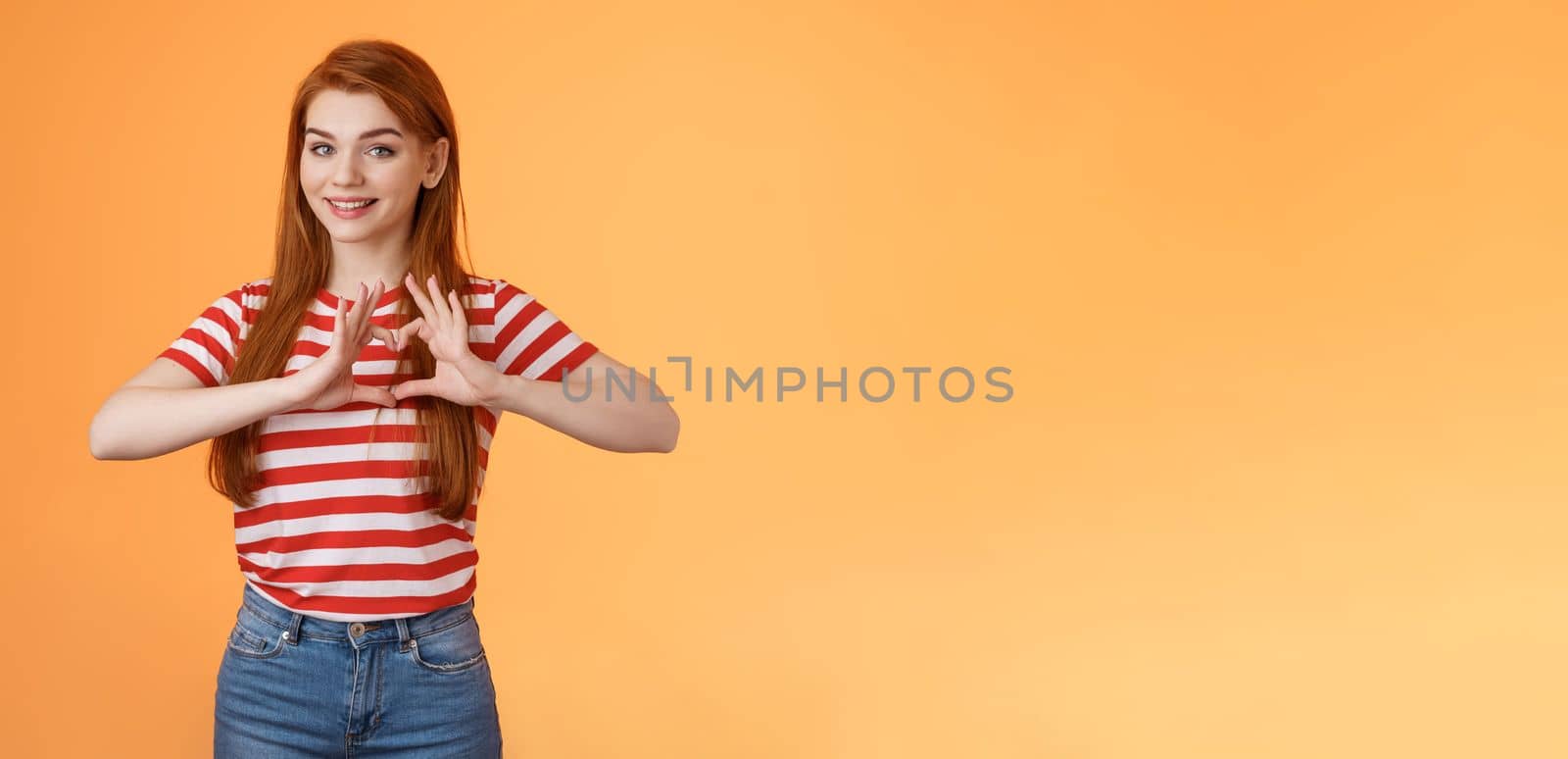 Cute lovely cheerful redhead girlfriend express love and cherish relationship, celebrating anniversary show heart sign, smiling tenderly, confess sympathy, stand orange background by Benzoix