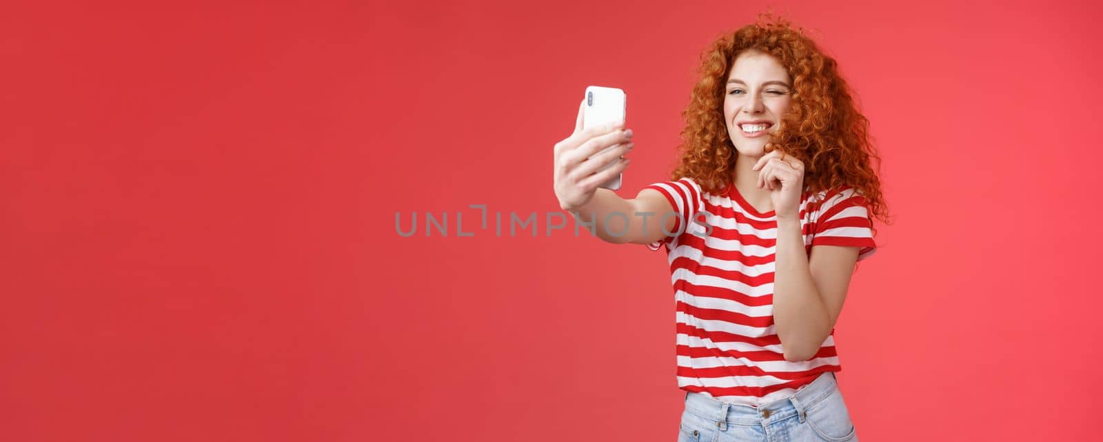 Lifestyle. Sassy good-looking stylish charismatic redhead female curly hairstyle winking cheeky expression making flirty kinky faces hold smartphone taking selfie record video message play funny facial filters.