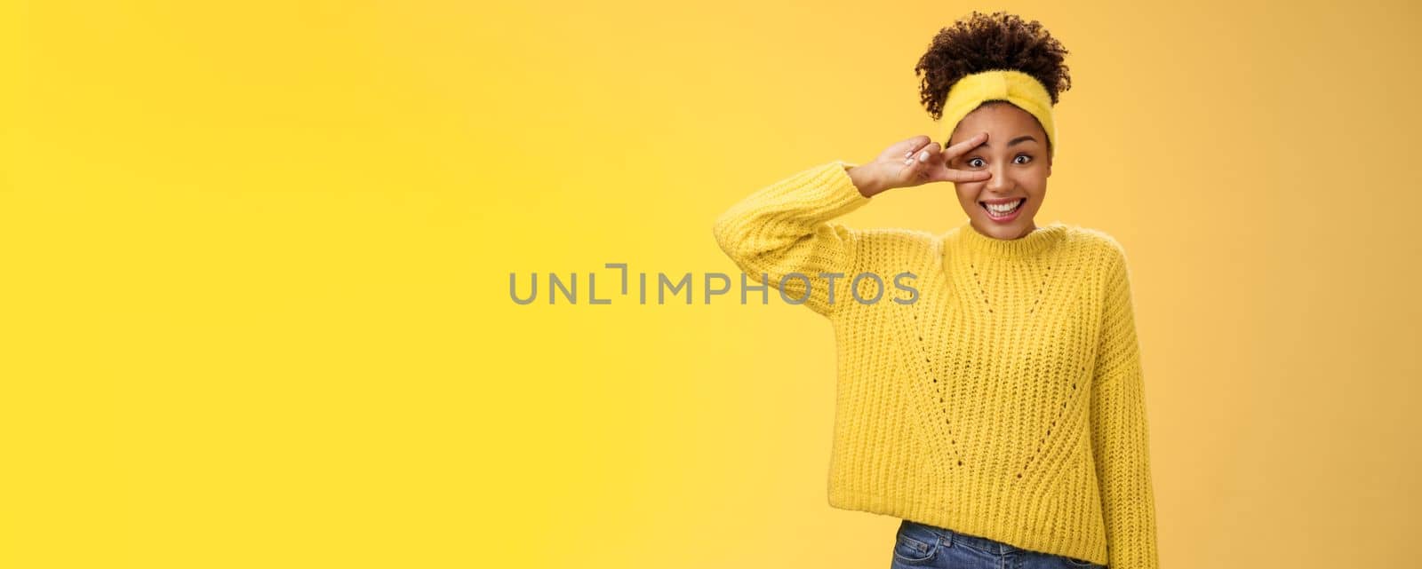 Silly insecure cute awkward young millennial girl blushing unconfident photographing smiling show peace victory sign near eye bad in posing, standing friendly yellow background. Copy space