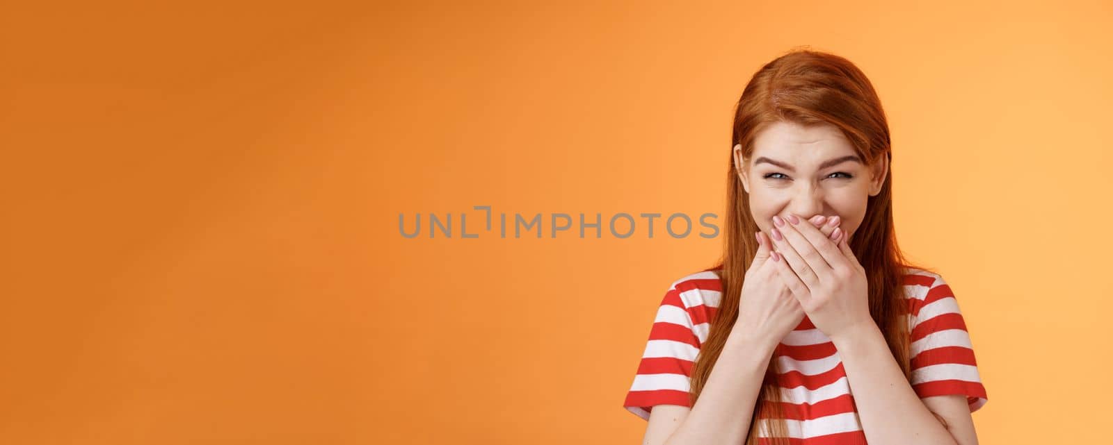 haha very funny. Silly tender cheerful redhead girl laughing, giggle hilarious joke, cover mouth press palms lips chuckling silent, mocking friend, stand upbeat orange background. Copy space