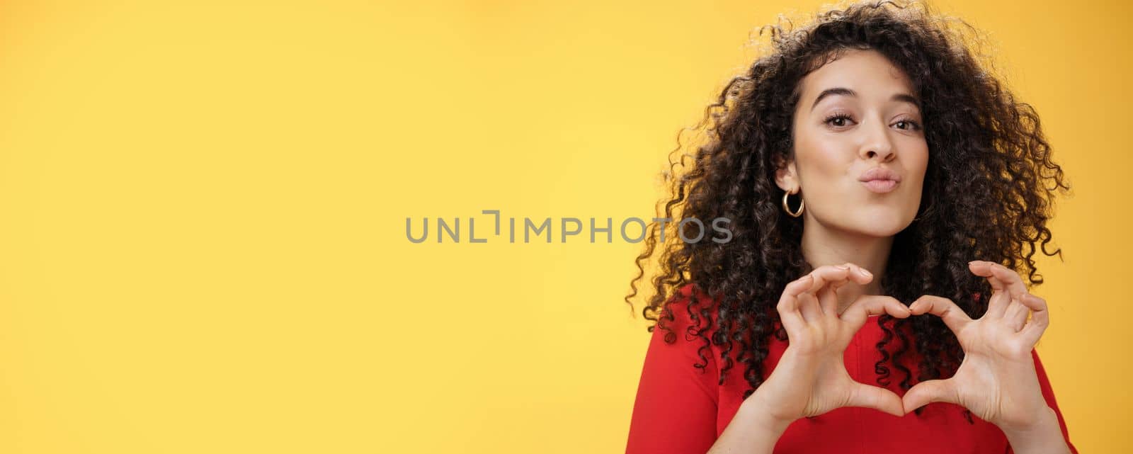 Close-up shot of romantic and tender young girlfriend with curly hair folding lips in kiss or mwah showing heart gesture, expressing love and romance, confessing in admiration or sympathy. Relationship, holidays and facial expressions concept