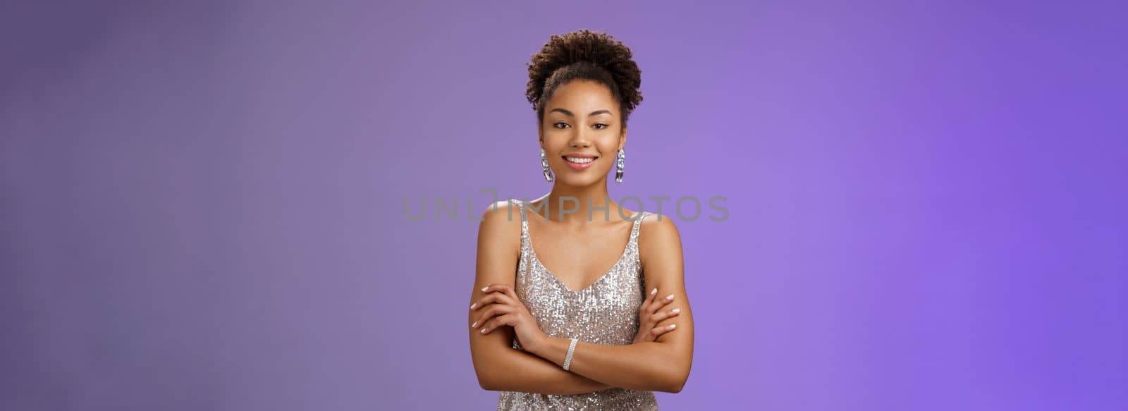 Confident wealthy attractive african. woman in silver luxurious night dress hold hands crossed chest self-assured mighty pose smiling broadly enjoying rich life standing bossy blue background rejoice.