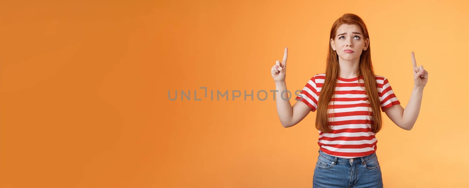 Hesitant upset cute redhead woman weighing choices look doubtful uncertain, frowning thoughtful, ponder decision, look pointing up unsure, have doubts, stand insecure orange background by Benzoix