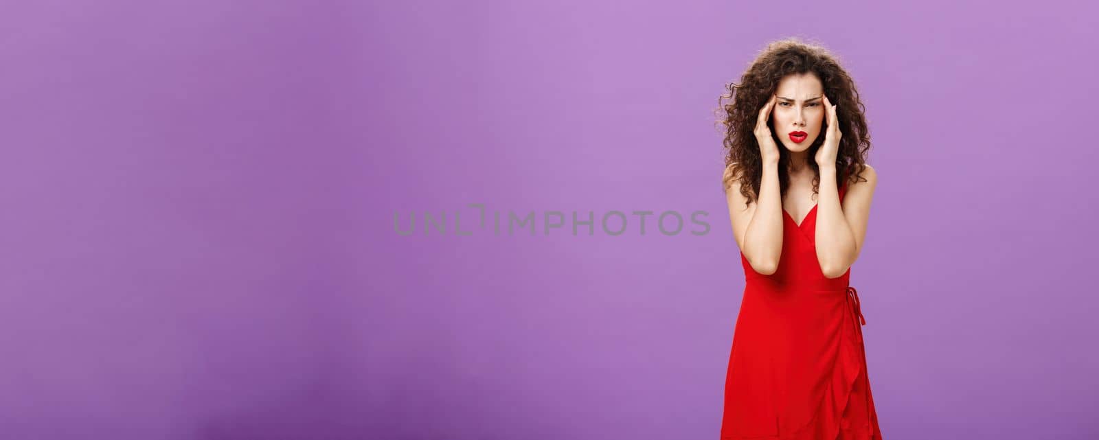 Stupid people getting on her nerves. Irritated and bothered stylish rish businesswoman in evening red dress pulling corners of eyes aside staring annoyed and unfocused at camera over purple background by Benzoix