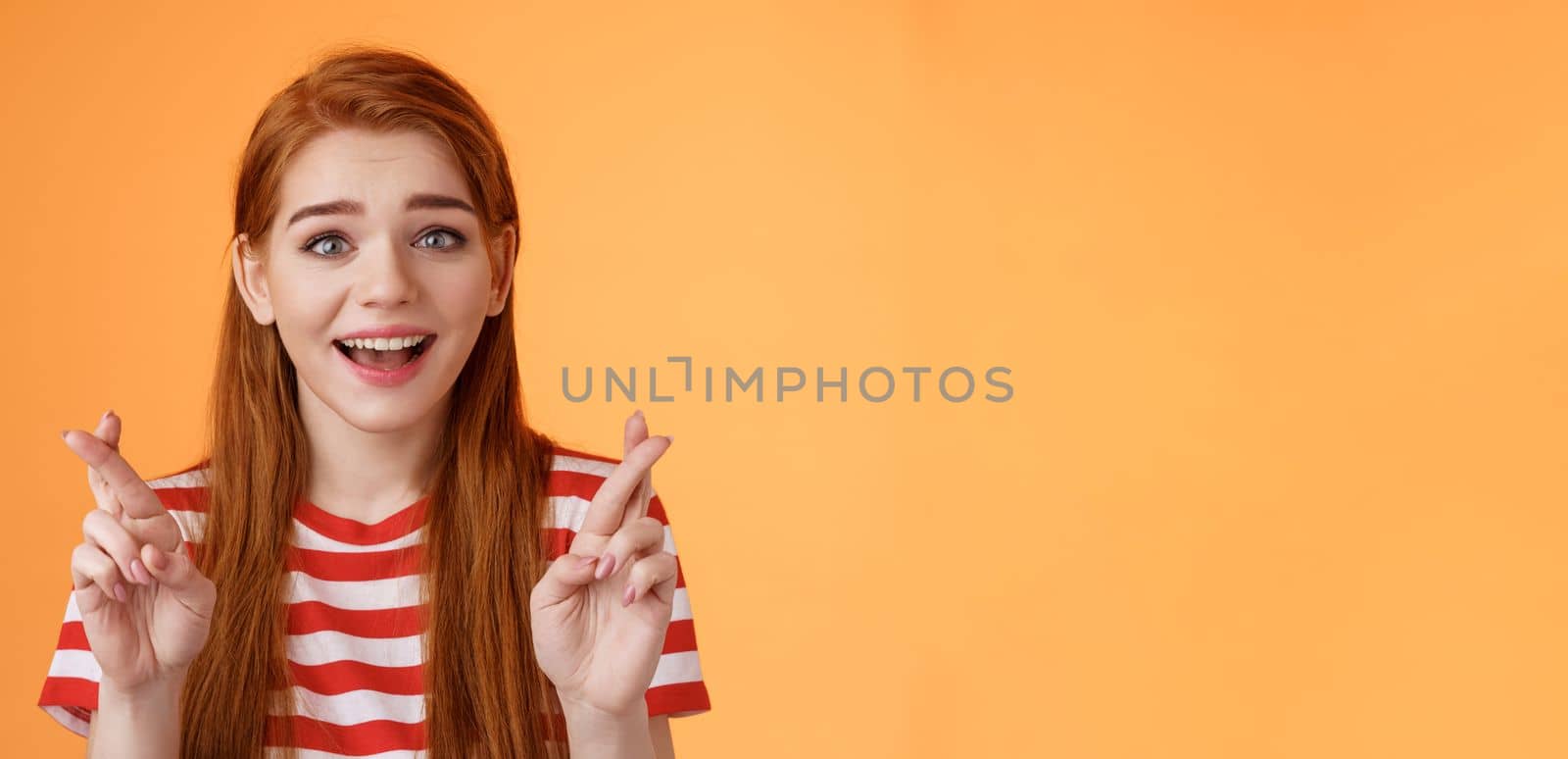 Excited hopeful redhead girl hope win lottery, smiling optimistic, look faith, believe dream come true, cross fingers good luck, make wish, anticipate good news, praying fortune, orange background.
